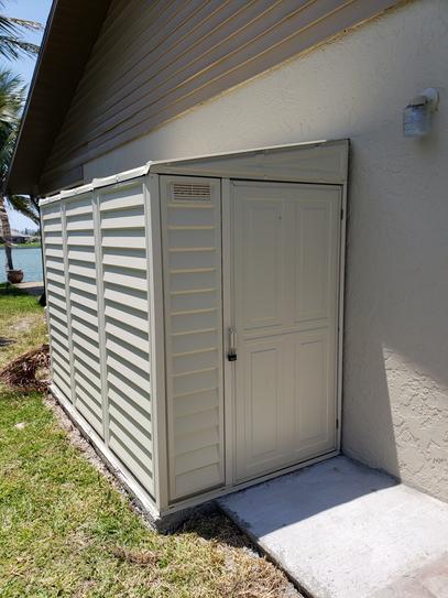 Duramax 06625 SideMate Shed 4'x8' installed beside a lakeside house, partially shaded and placed on a concrete slab.
