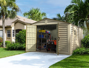 Large beige Duramax Woodbridge Plus 10.5'x13' shed, open and full of tools and storage shelves, set in a lush green yard beside a residential home.