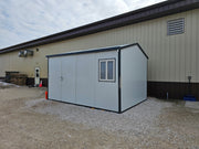 Angled view of Duramax 13'x10' Insulated Glass Building - 32003 with a gabled roof and placed alongside an industrial warehouse.

