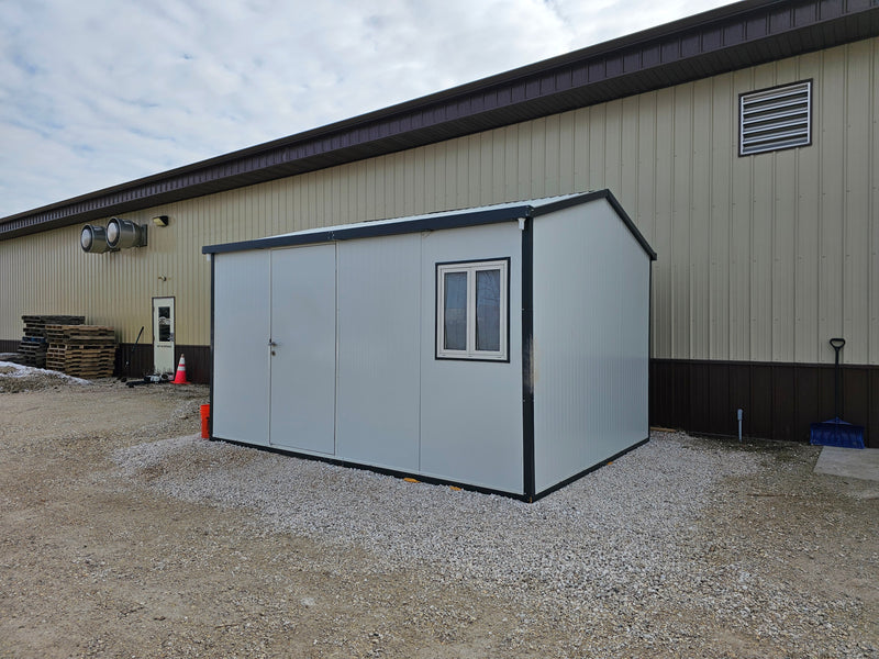 Angled view of Duramax 13'x10' Insulated Glass Building - 32003 with a gabled roof and placed alongside an industrial warehouse.


