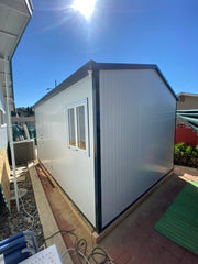 Backyard placement of Duramax Insulated Glass Building 13'x10' - 32003 next to a house, with visible roofing and a sunny sky.