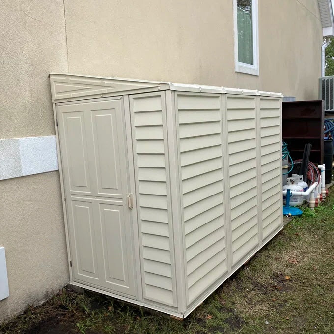 Duramax model 06625 SideMate Shed 4'x8' mounted on a wooden base beside a tan residential building.