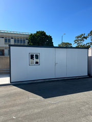 Front view of Duramax 13'x10' Insulated Glass Building set in an institutional parking area, with clear blue sky above.