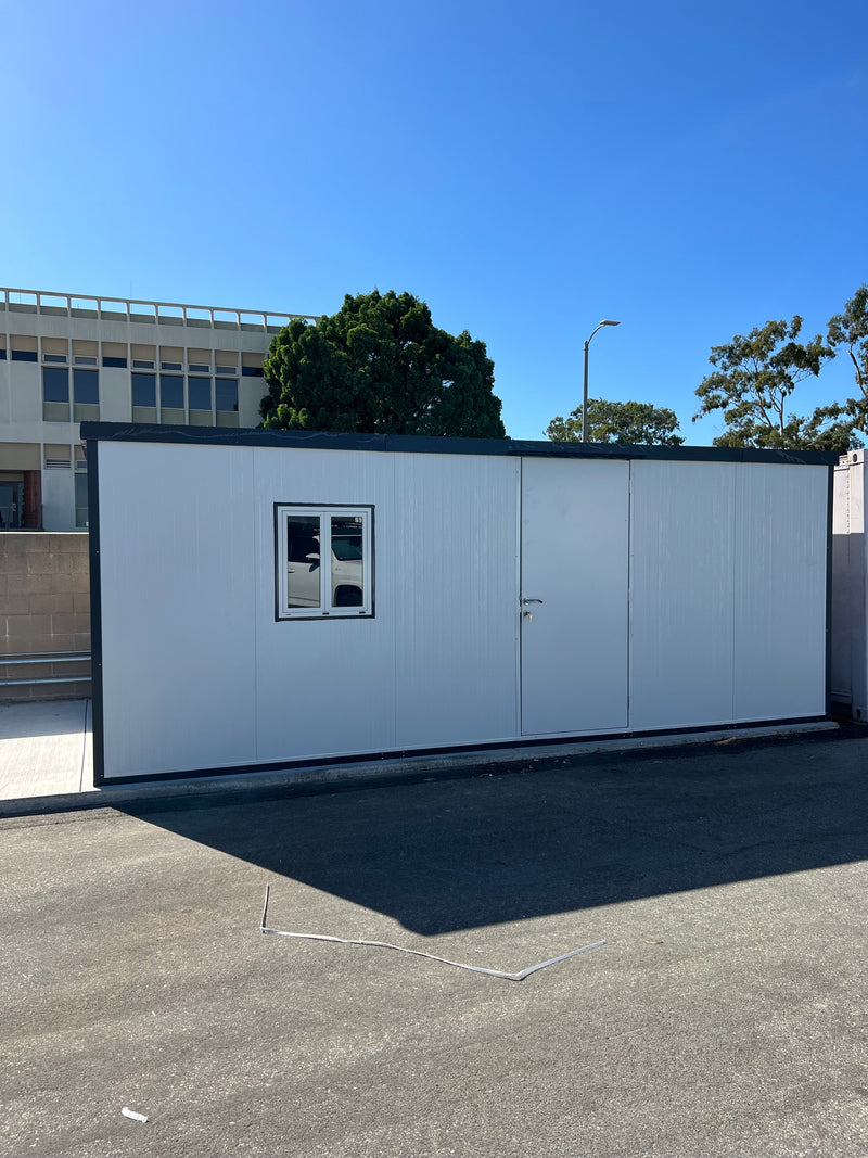 Front view of Duramax 13'x10' Insulated Glass Building set in an institutional parking area, with clear blue sky above.