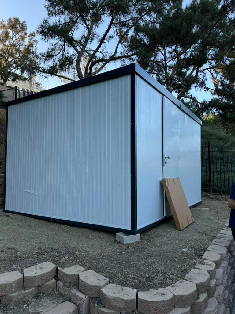Duramax Insulated Glass Building 13'x10' - 32003 installed on a sloped yard area with retaining wall and surrounding trees.