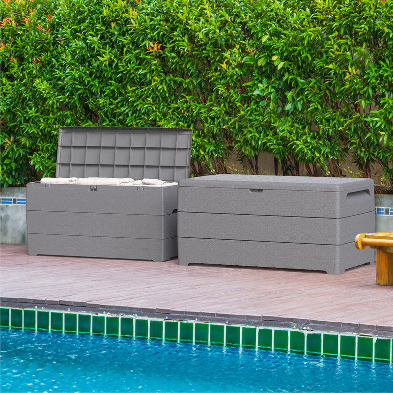Two Duramax 71 Gallon Outdoor Storage Boxes in Gray, by the poolside with lush greenery in the background.