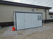 Duramax Insulated Glass Building 13'x10' installed on gravel with orange bucket in front of a beige industrial building.