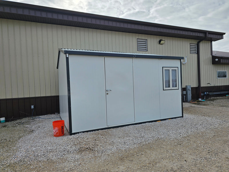 Duramax Insulated Glass Building 13'x10' installed on gravel with orange bucket in front of a beige industrial building.