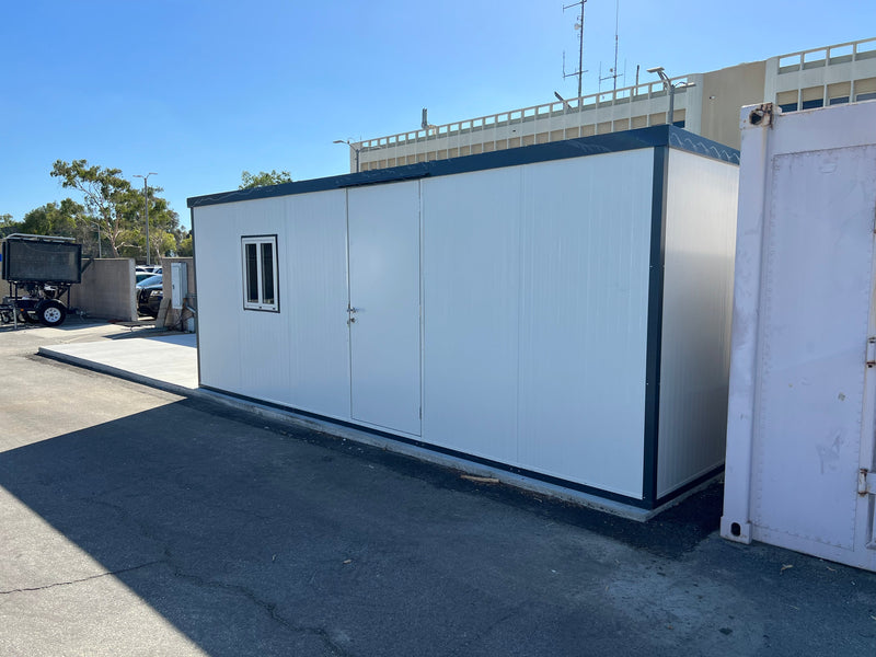 Side perspective of Duramax Insulated Glass Building 13'x10' placed in a paved lot near containers and trailers.