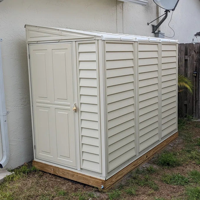 Side view of a Duramax SideMate Shed with Foundation 4'x8' (model 06625) placed beside a stucco house wall with a padlock on the door.

