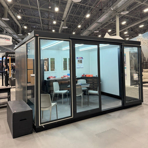 Interior view of a trade show setup featuring the Duramax Insulated Glass Building 13'x10' - 32003 with glass panels, chairs, and a table.